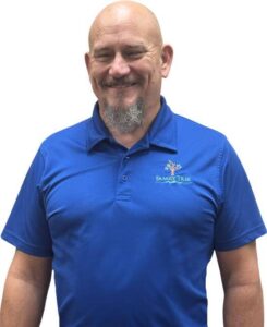 Dr. Micah Carter smiling looking professional wearing a blue polo with Family Tree Chiropractic emblem