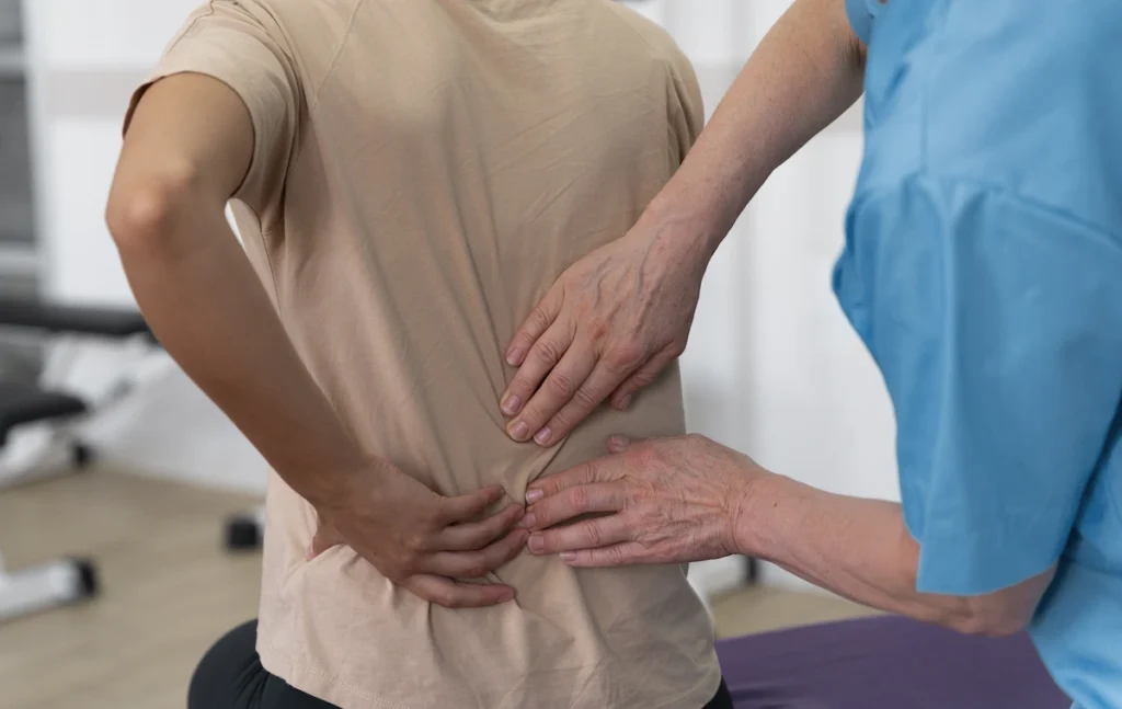 Woman with sciatica pain holding her lower back from the pain while chiropractor assesses it