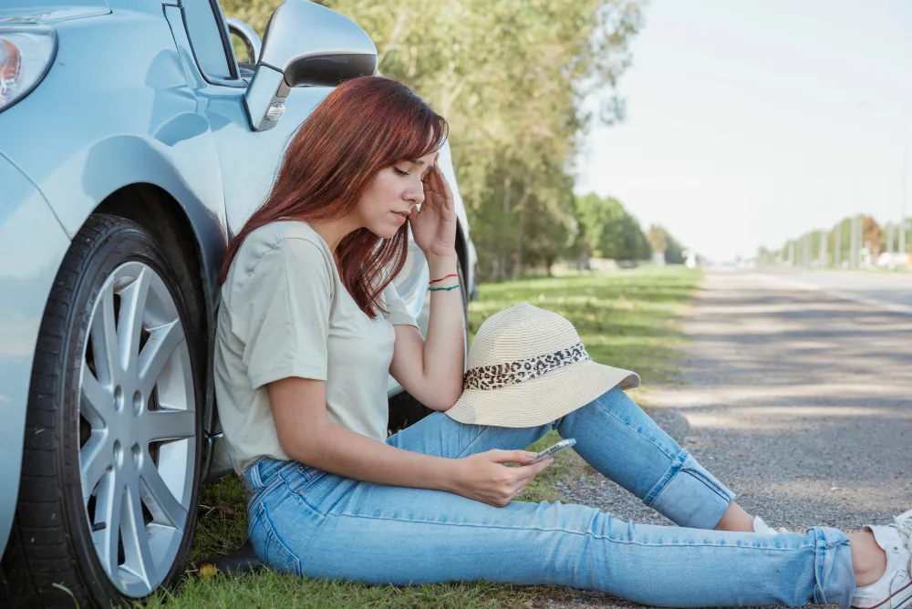 Woman sitting beside her car experiencing symptoms after a car accident