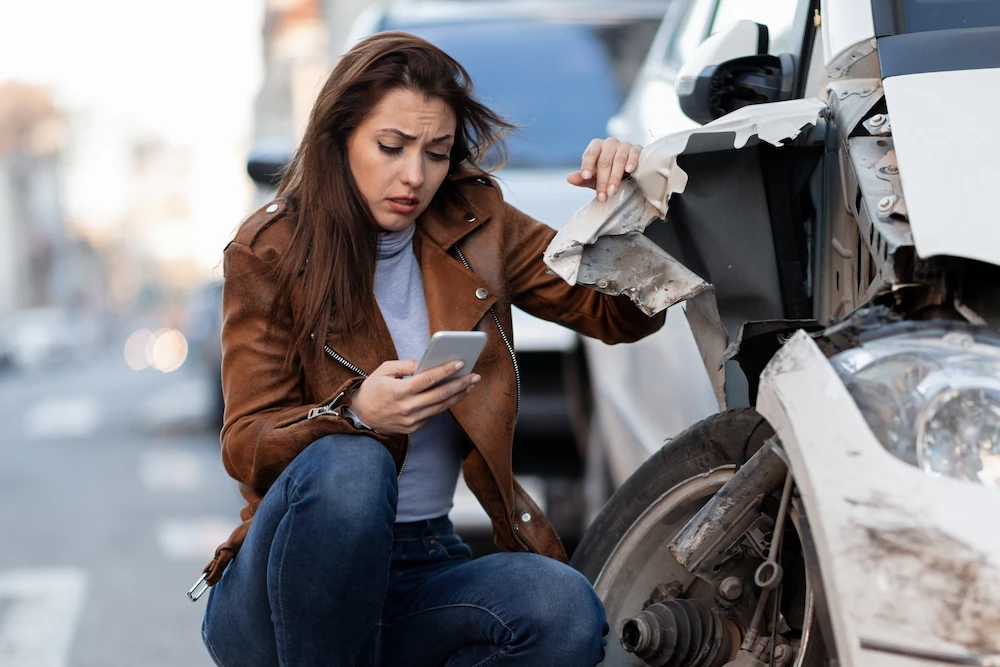 Person sitting beside damaged car after accident without visible injury symptoms